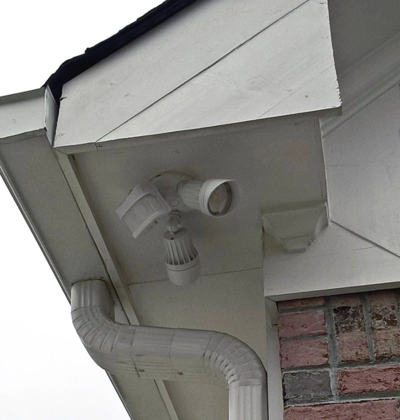 LED motion sensor wall fixture with integrated PIR sensor head and adjustable sensitivity dial mounted on exterior siding